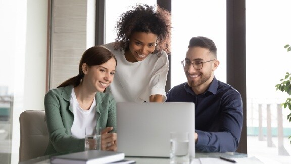 Group of employees smiling while working on a laptop in an office