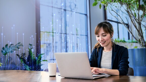 Female employee working on her laptop in office, overlaid with a graphic of transmission nodes in the backgroound