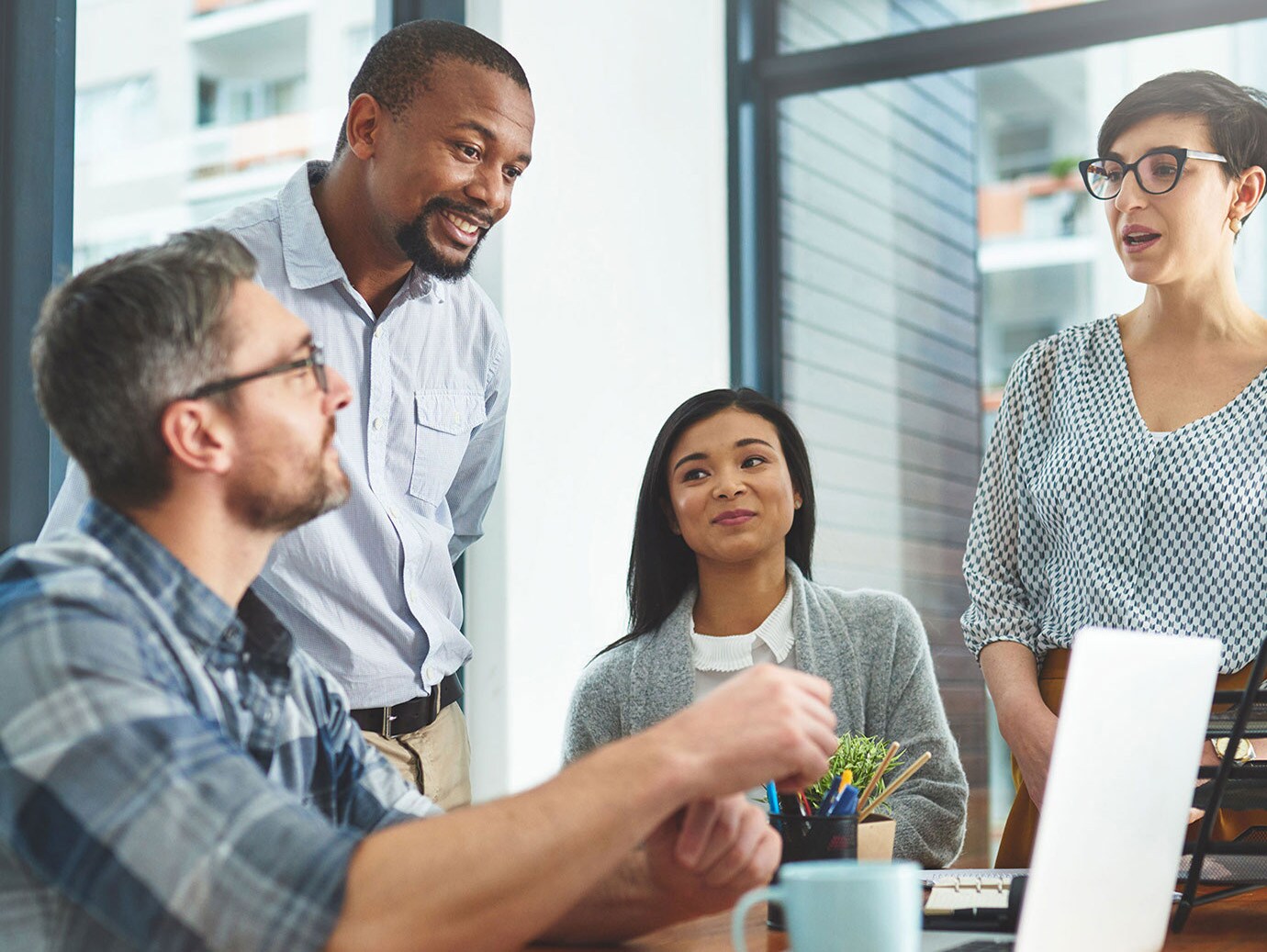 Four colleagues in discussion in front of a laptop on a table