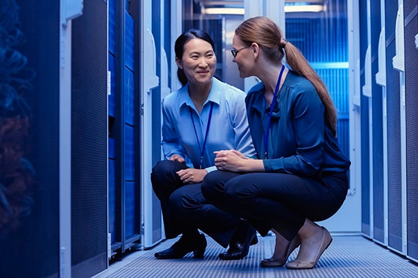 Two female engineers kneeling down and having a conversation in a data center