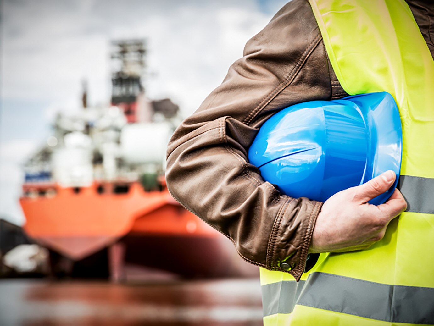 Man in uniform holding a blue safety helmet in front of a ship