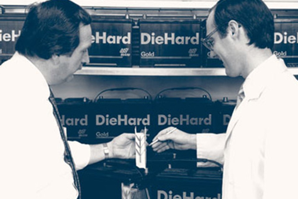 Two men standing and looking at DieHard Gold Batteries displayed on racks