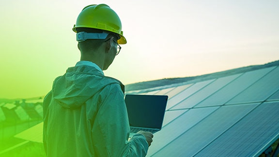 Man wearing a safety helmet working on a laptop in a solar power plant
