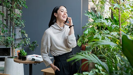 Woman smiling while having a conversation on her phone, surrounded by indoor plants in room