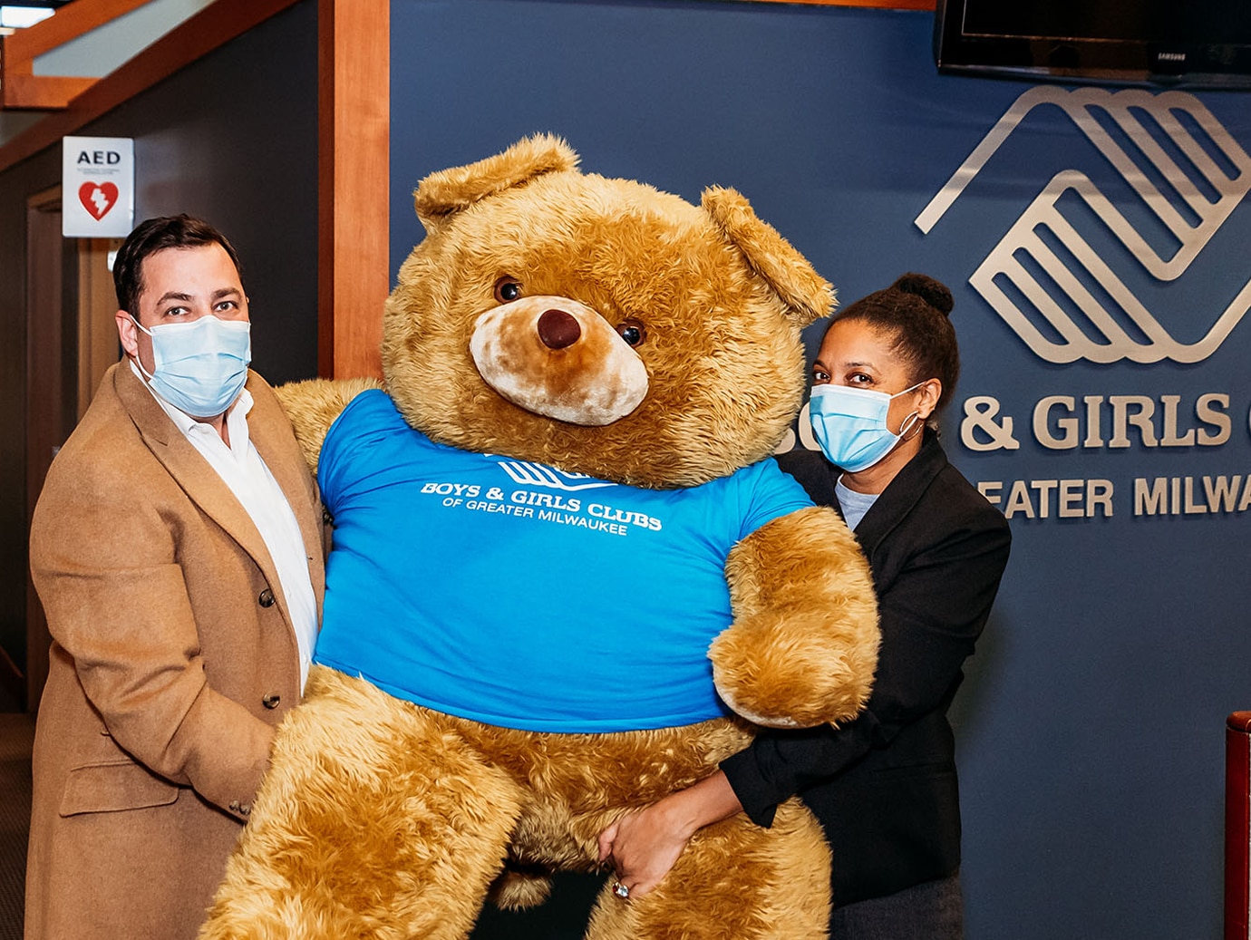 Man and woman posing with a teddy bear to promote Boys anf Girls club of Greater Milwuakee