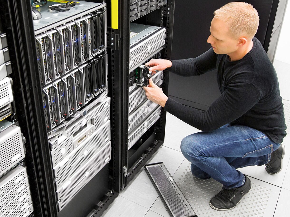 Technician kneeling in front of a data rack, inspecting it
