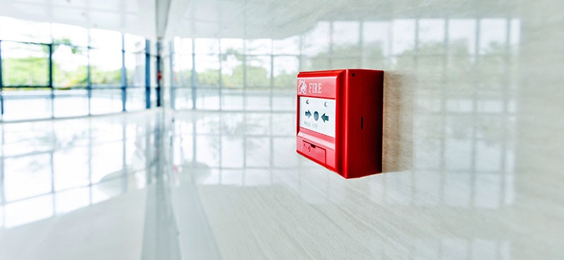 A red fire detection panel mounted on a white wall in a commercial building.