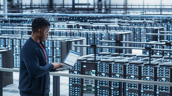 An engineer standing in front of data racks using a laptop