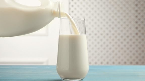 Close-up shot of pouring fresh milk into a glass against white background