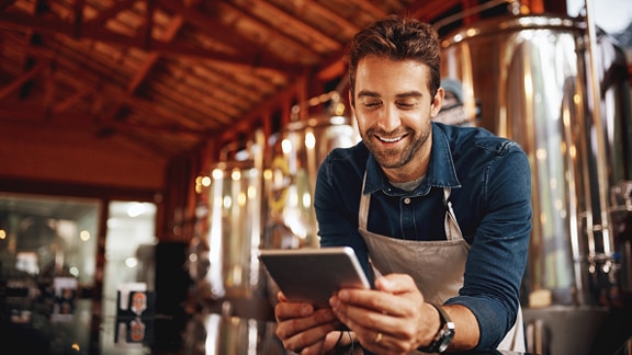 Man smiling looking at a tablet standing at the bar at a brewery