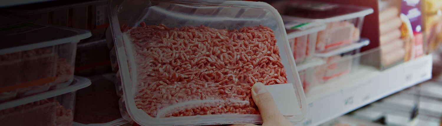 Close-up of a person holding a box of processed meat in a supermarket