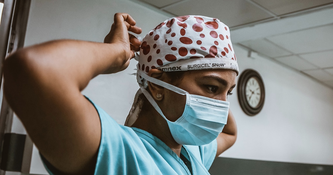A doctor in scrubs tying a surgical cap