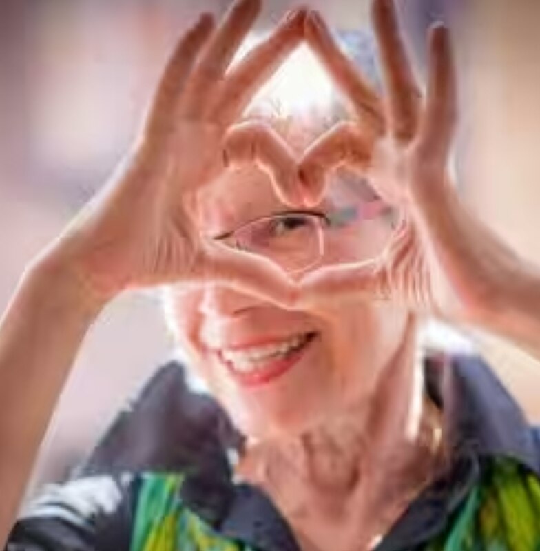 An elderly lady smiling and joining her hands to form a heart 