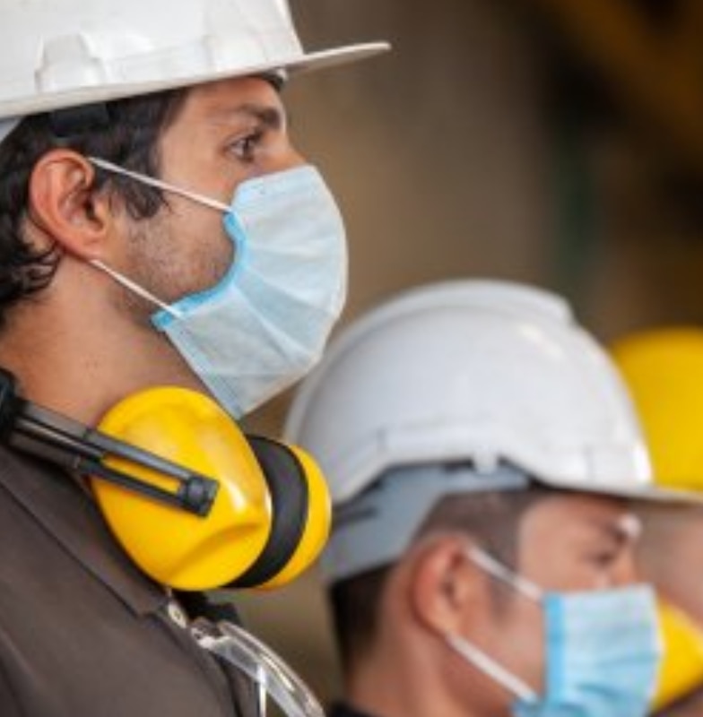 Three maintenance engineers wearing safety gear and face-masks, standing in a line