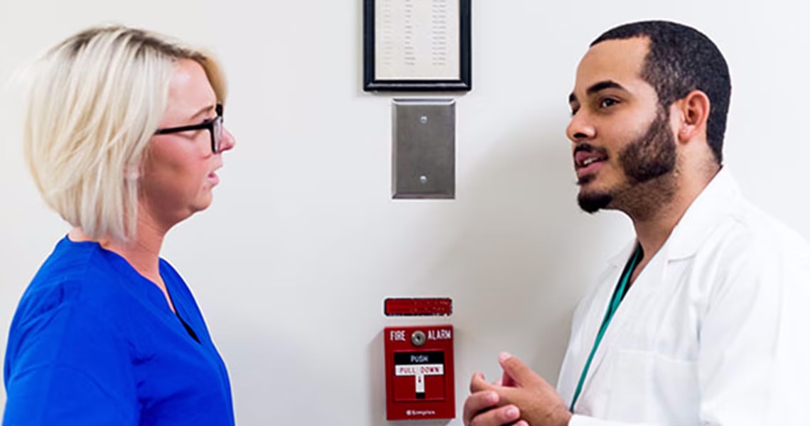 Two doctors talking next to an emergency fire alarm switch