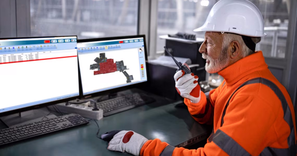 Man in safety gear working on two monitors and using a handheld transceiver