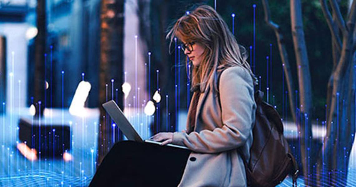 A woman wearing a backpack and working on a laptop