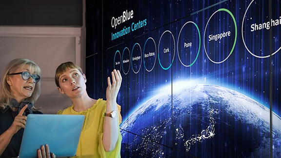 Two women discussing Openblue graphics being displayed on a smart screen