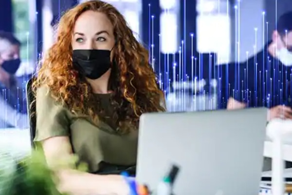 Woman wearing a face mask working in office, overlaid with a graphic of transmission nodes