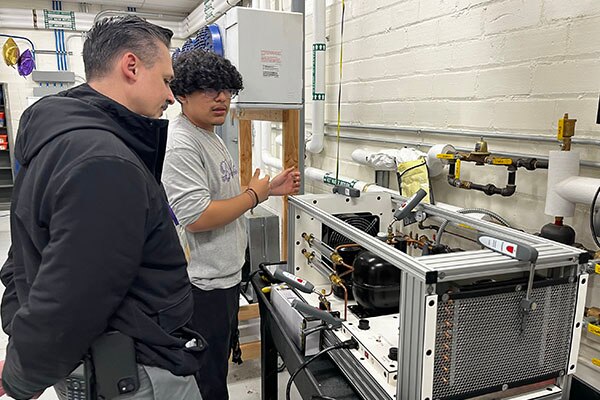 A Waukegan High School student explains some of what they are learning in the new HVAC lab to an event attendee 