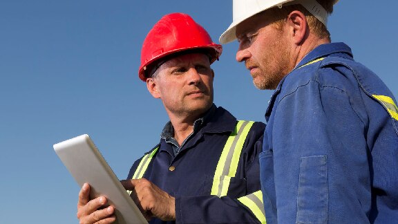 Two maintenance workers discussing, while one holds a screen-tablet