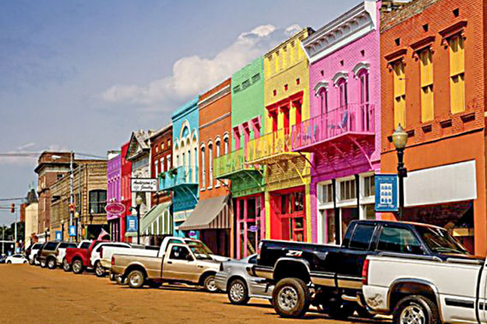 A series of colorful buildings and cars parked in front of them at Downtown Yazoo, MS