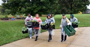 Group of volunteers in raincoats carrying crates full of of vegetables
