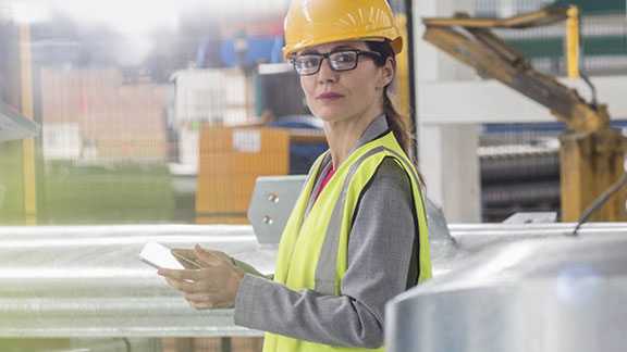 Female worker in a safety helmet using a tab in a factory