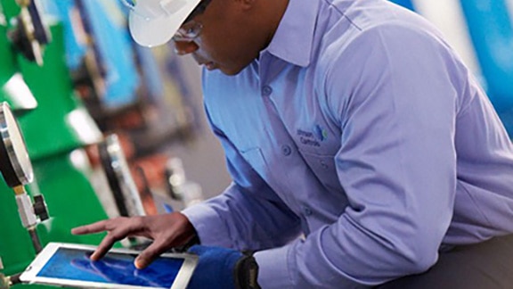 Man in Johnson Controls safety equipment using a tablet in front of machines with modern graphics