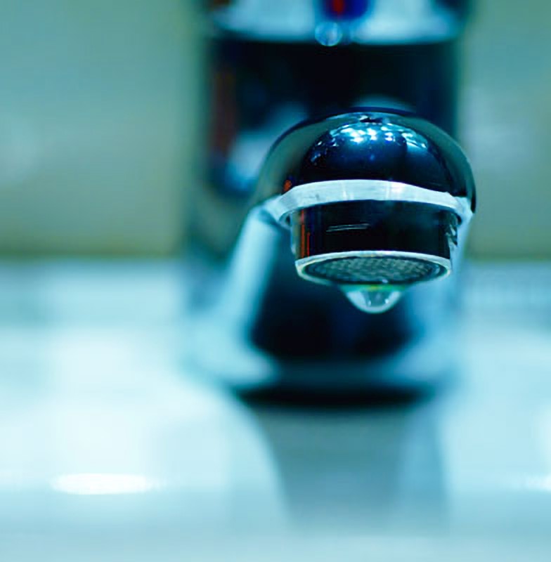 Close-up of a tap of a sink, with a drop of water leaking from it