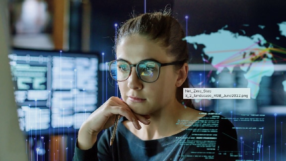 Close-up of a woman wearing glasses and looking at a monitor, with OpenBlue graphics in the background