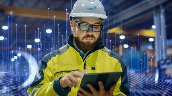 A maintenance engineer scrolling on a tablet, surrounded by OpenBlue graphics