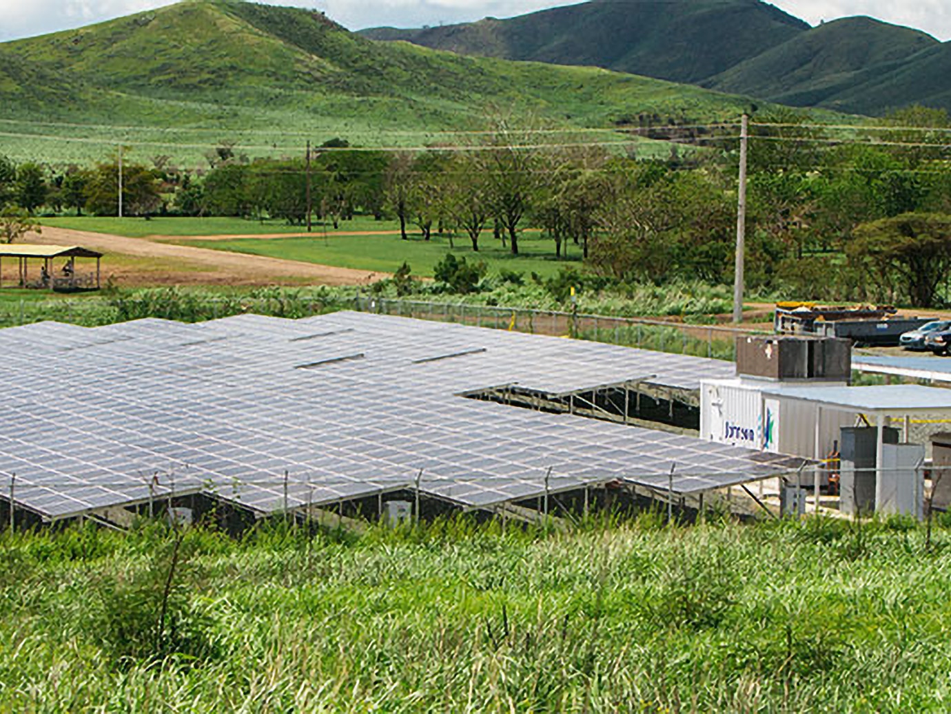 Solar panels set up in a grassy field with lush hills in the background