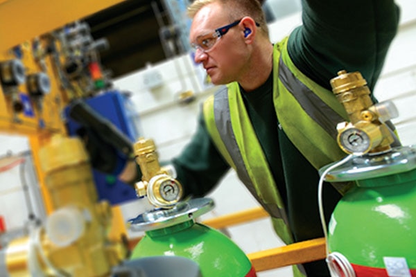 A man in safety equipment with green fire extinguishers in the foreground